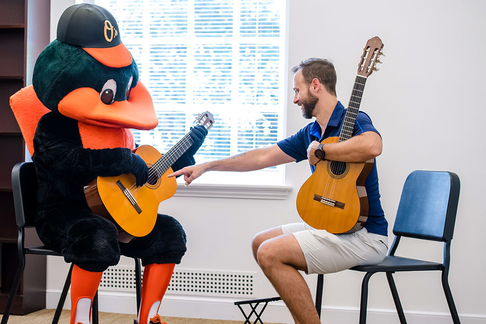 Baltimore School of Music owner and CEO James Lowe teaches the Oriole Bird how to play the guitar during a school open house.