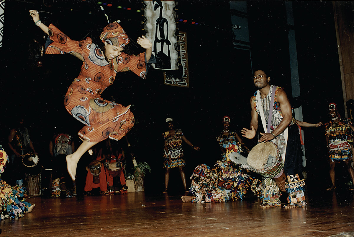 Olu Butterfly Woods leaps as King Salim Ajanku drums, at the Sankofa Center for Cultural Enrichment performance with Ibeji masks, c 2004-2005_photo by Armeta La Verne Gray_CMYK
